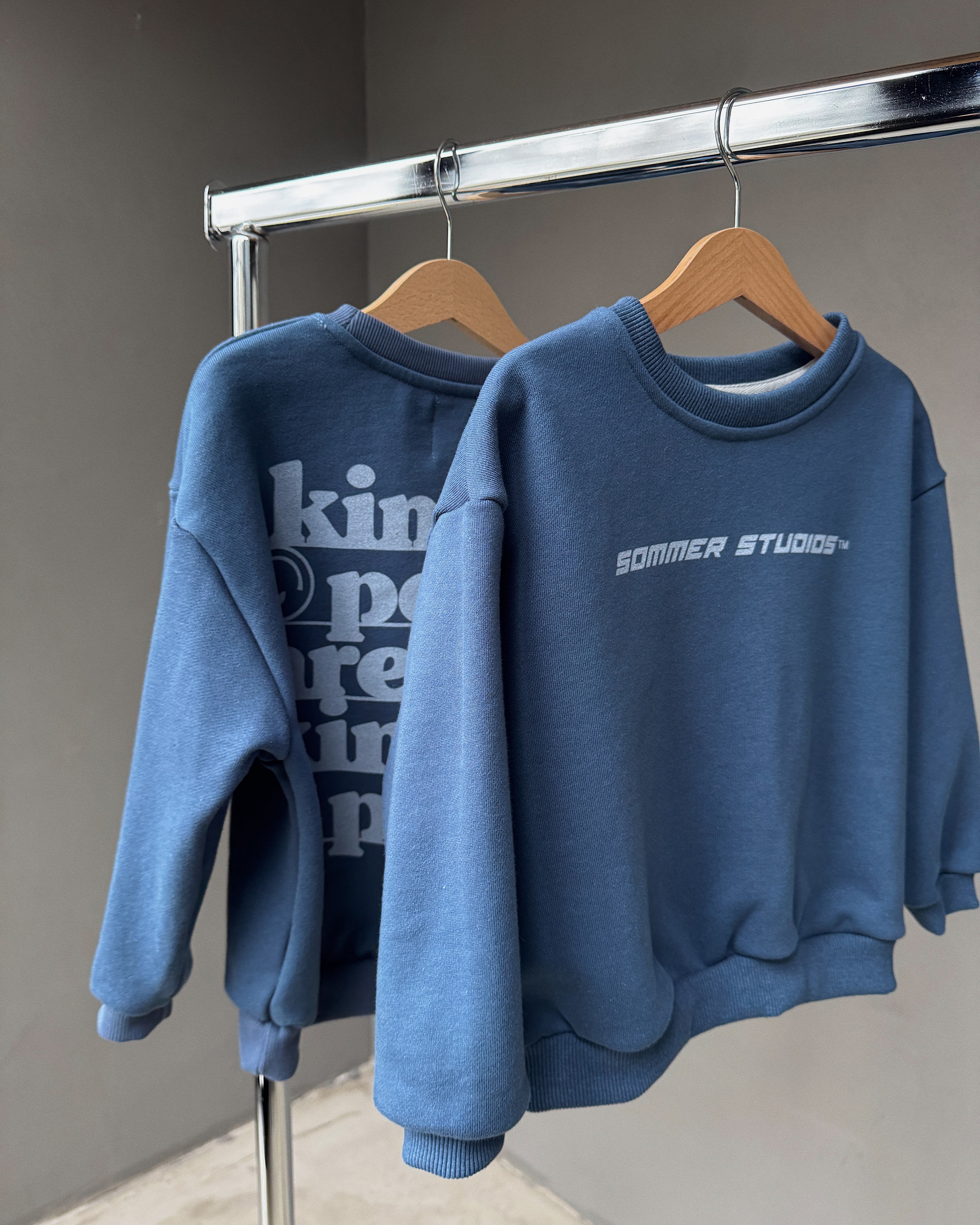 Two blue sweatshirts hanging on a rack with visible branding.
